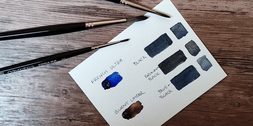 Sample card of black paints lying on a desk top with paint brushes beside it