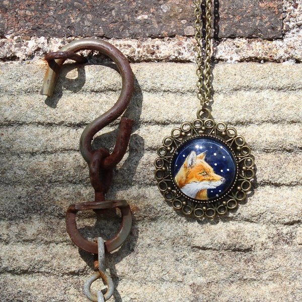 Hand painted fox pendant hanging on a stone wall beside a rusty hook