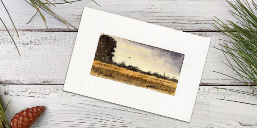 Watercolour painting of an evening sunset in greys and golds lying on a desk top